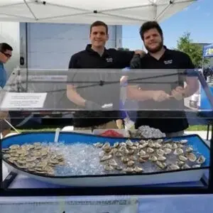 Two men standing next to a display of oysters.