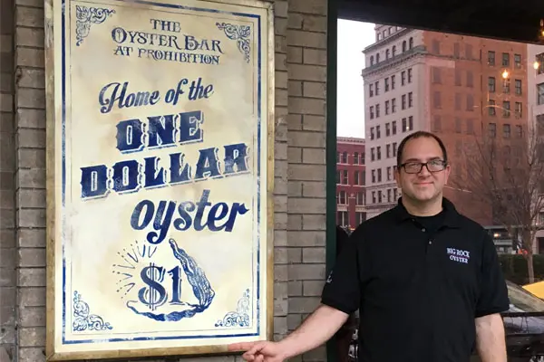 A man standing next to a sign that says " the oyster bar at furnishore ".